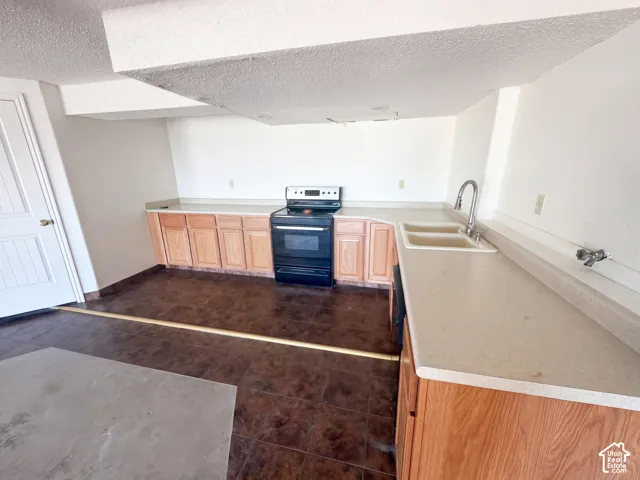 Kitchen featuring wood cabinetry, integrated countertops, a black range, and a double-basin sink with a high-arch faucet, complemented by tile flooring
