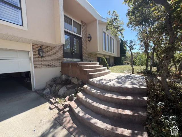 Exterior facade featuring multi-tone brick and stucco siding, double-door entryway, tiered stone-paver steps, and integrated exterior sconce lighting
