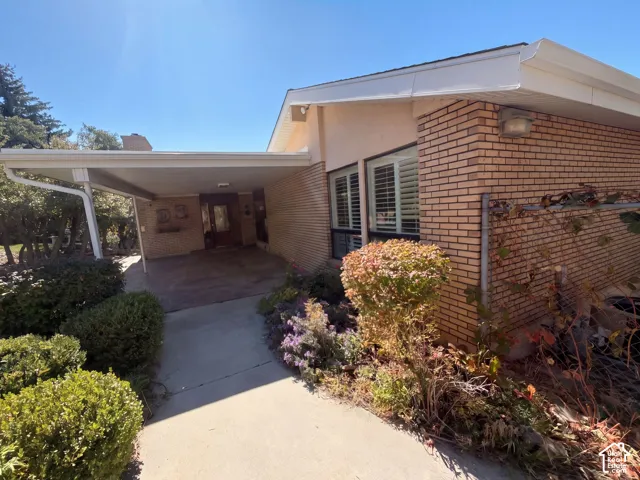 Ranch-style exterior featuring a brick facade, covered carport, concrete walkway, and window shutters