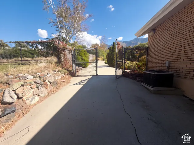 Concrete driveway featuring a metal security gate, brick exterior siding, and a mountain backdrop