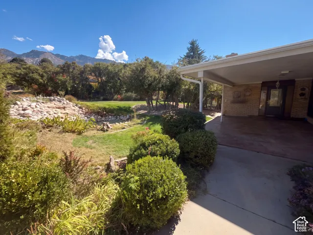 Brick exterior with a covered patio, tiered stone landscaping, manicured lawn, and mountain backdrop