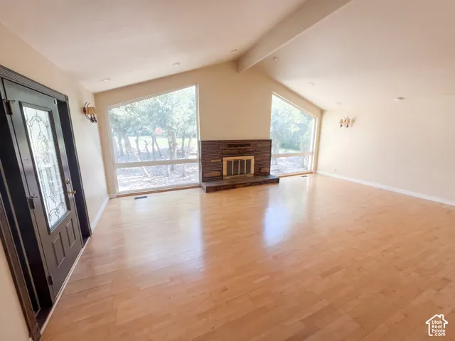 Vaulted ceilings, wood-finish flooring, masonry fireplace with a raised hearth, oversized trapezoidal windows, and a decorative glass-panel front door