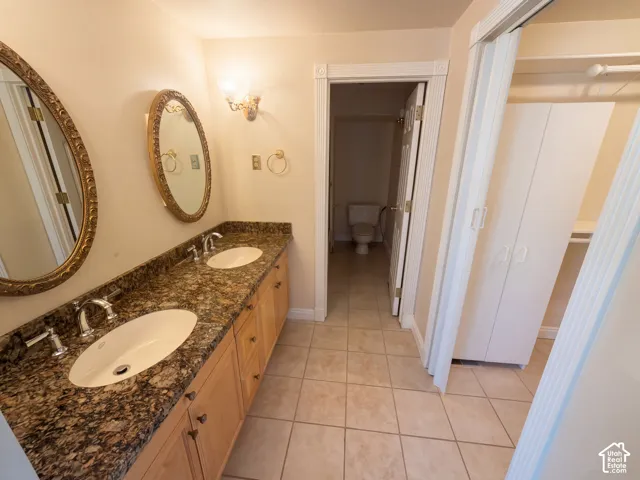 Dual-vanity bathroom featuring stone-surfaced countertops, oval drop-in sinks, light-finish wood cabinetry, and ceramic tile flooring