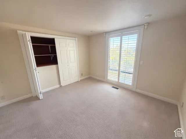 Neutral interior space featuring wall-to-wall carpeting, recessed lighting, white louvered shutters, and a closet with bifold doors and built-in shelving