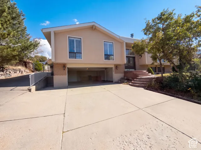Stucco and brick facade featuring an integrated garage, concrete driveway, and curved stone steps leading to the main entrance
