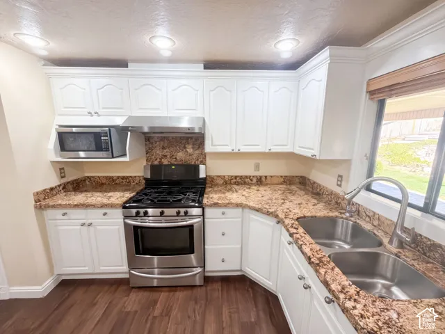 Kitchen featuring white cabinetry, stone-patterned countertops, stainless steel gas range, built-in microwave, and wood-finish flooring