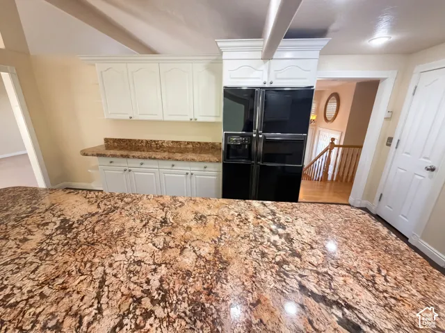 Kitchen featuring white shaker-style cabinetry, expansive stone countertops, and a built-in black refrigerator