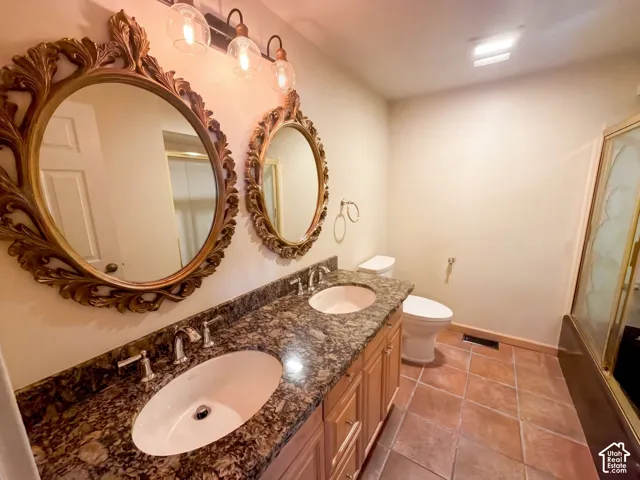 Dual vanity with stone-finish countertop, undermount sinks, wood cabinetry, and tile flooring