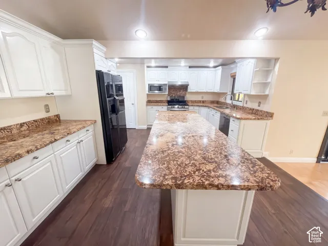 Kitchen featuring white cabinetry, stone-finish countertops, a central island, wood-finish flooring, and integrated appliances