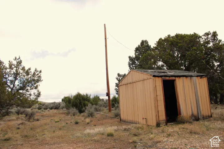Exterior outbuilding featuring metal siding and an open entryway, situated on a lot with native vegetation and a utility pole