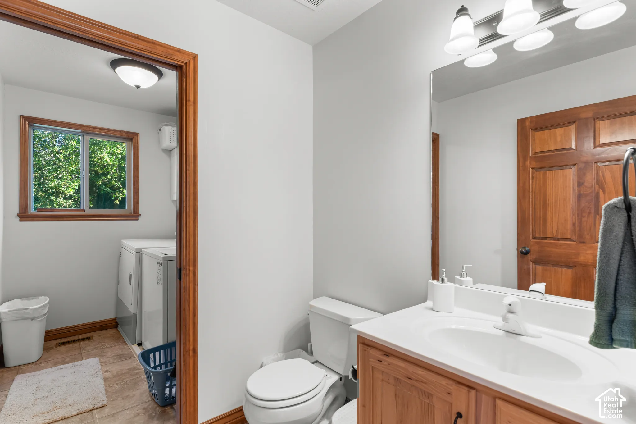 Bathroom featuring a wood-tone vanity cabinet, white countertop with integrated sink, large wall-mounted mirror, four-light fixture, and natural wood trim