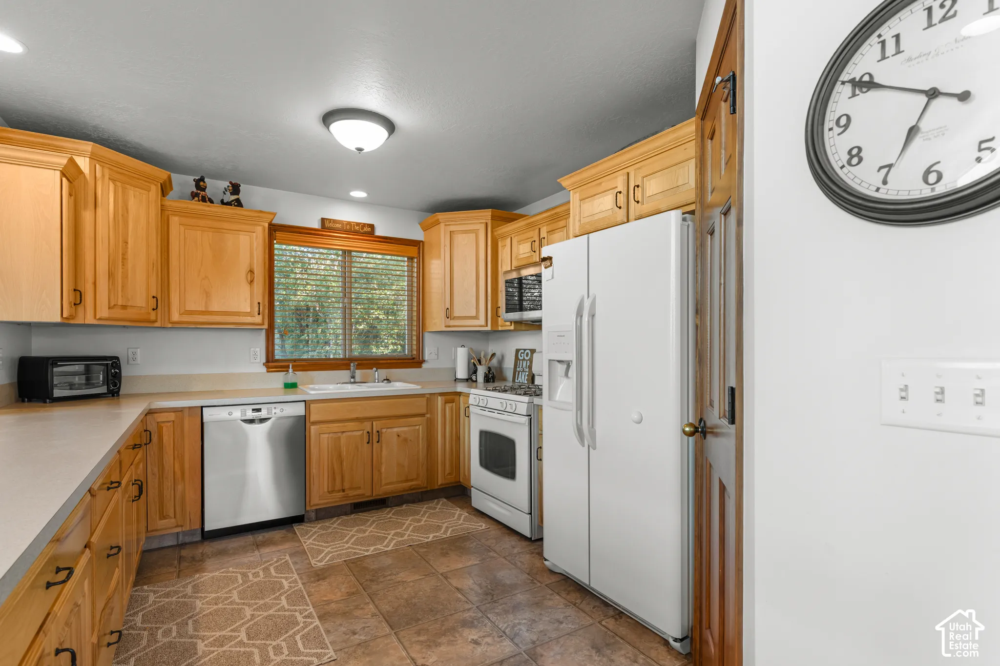 Kitchen featuring natural-finish wood cabinetry, solid-surface countertops, tile flooring, and stainless steel dishwasher