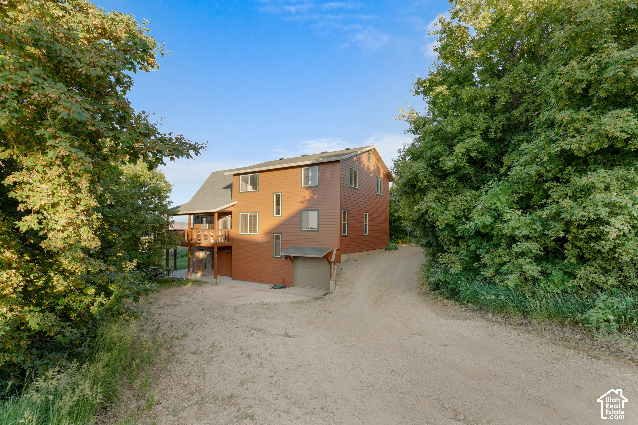 Three-story residence featuring horizontal siding, an attached garage, and a covered deck, situated on a secluded lot with dense mature landscaping