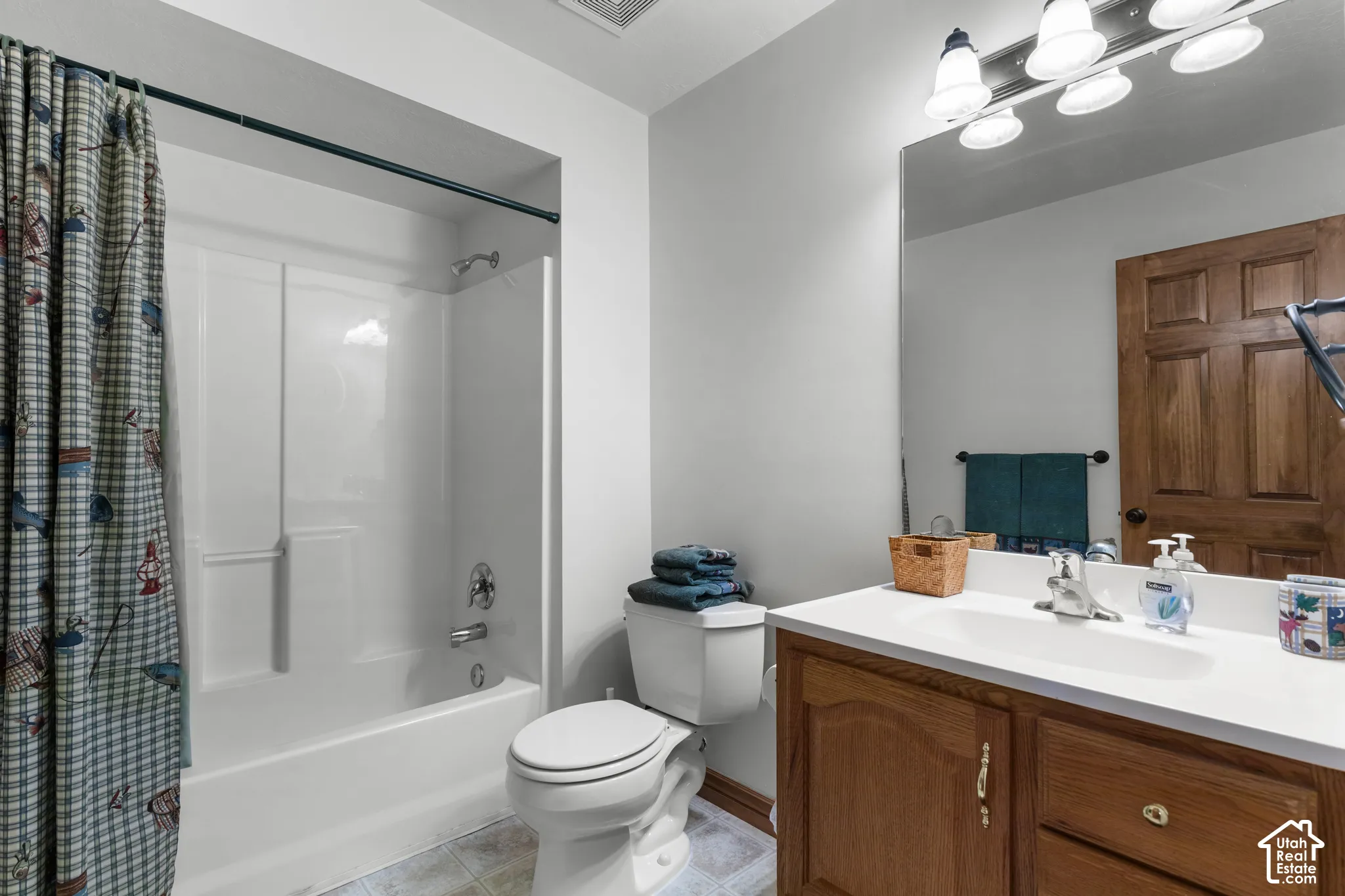 Bathroom featuring a white composite tub-shower combination, wooden vanity cabinetry with an integrated sink, expansive wall-mounted mirror, and multi-bulb vanity lighting
