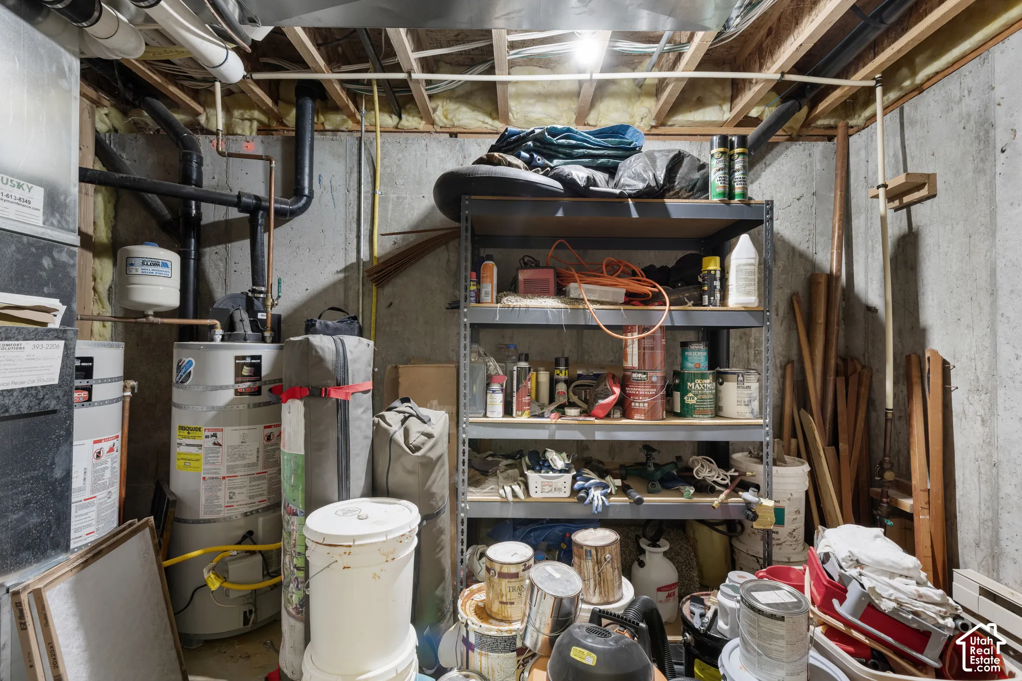 Utility area featuring poured concrete foundation walls, exposed ceiling joists, and a water heater