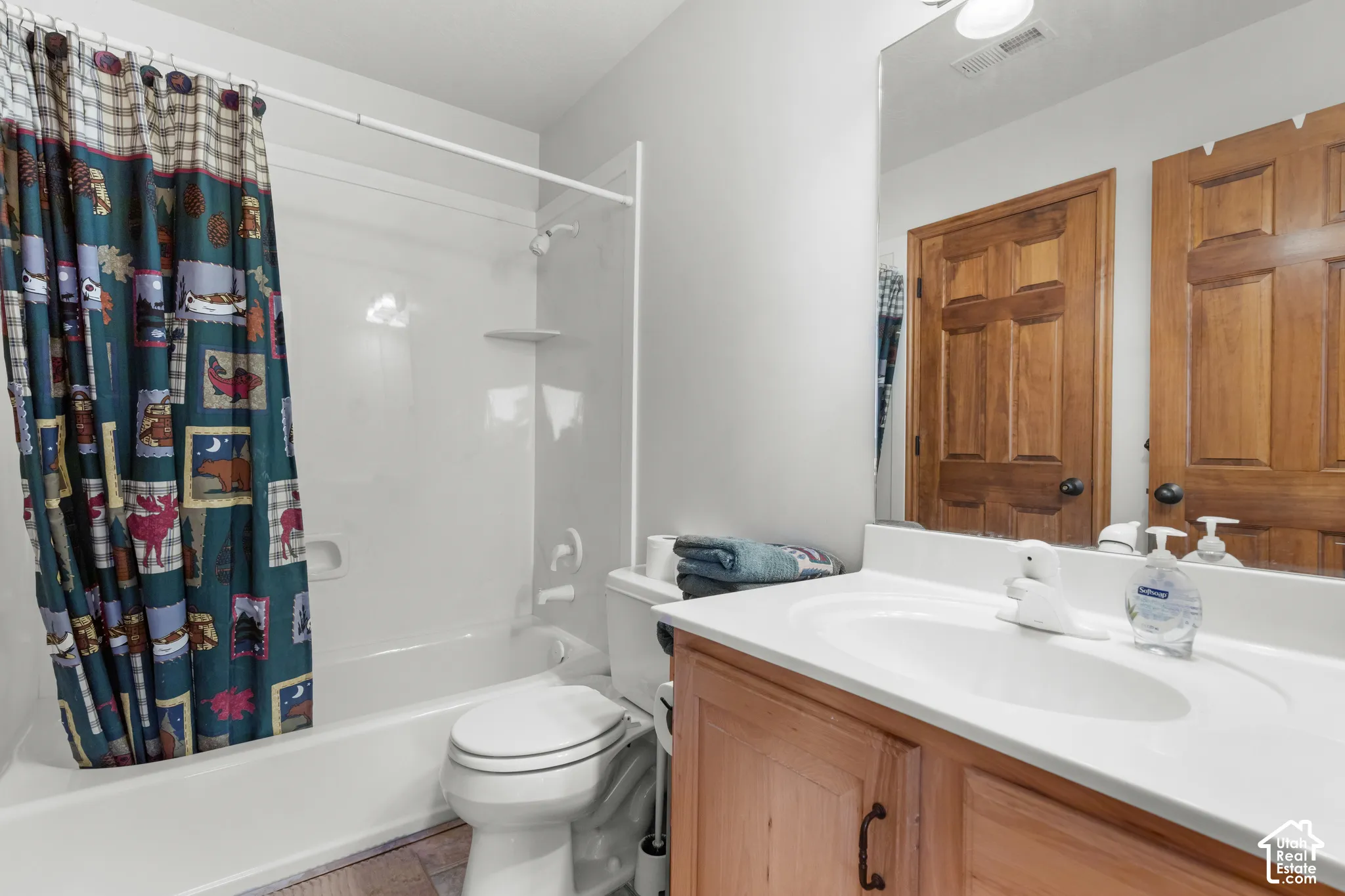 Bathroom featuring a vanity with a white countertop and integrated sink, wood-finish cabinetry, a large wall-mounted mirror, and a white tub-shower combination