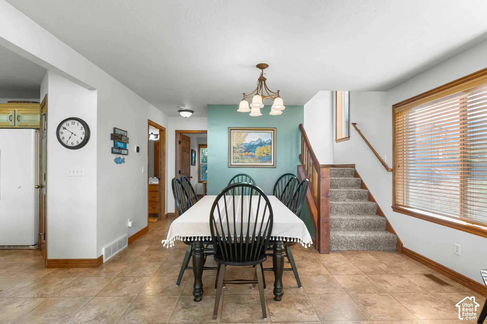 Open-concept dining area featuring neutral tile flooring, a multi-light chandelier, a prominent accent wall, and staircase with wooden handrail