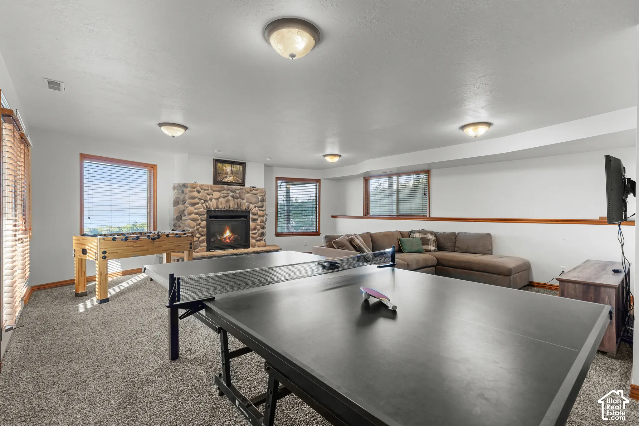 Floor-to-ceiling river rock fireplace, neutral wall-to-wall carpeting, multiple windows with wood-tone trim, and recessed and flush-mount ceiling lighting