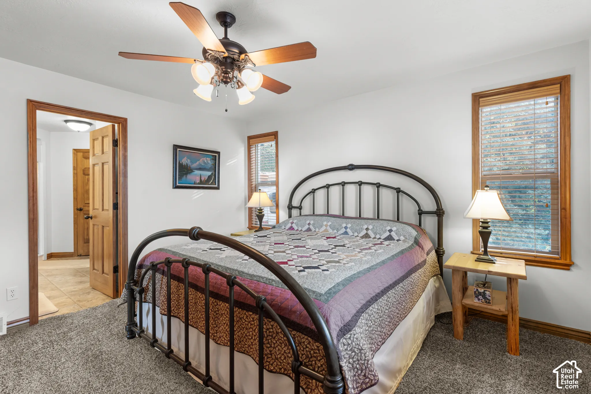 Neutral-toned carpeting, multi-pane windows with wood trim, six-panel wood door, and a ceiling fan with integrated multi-bulb lighting