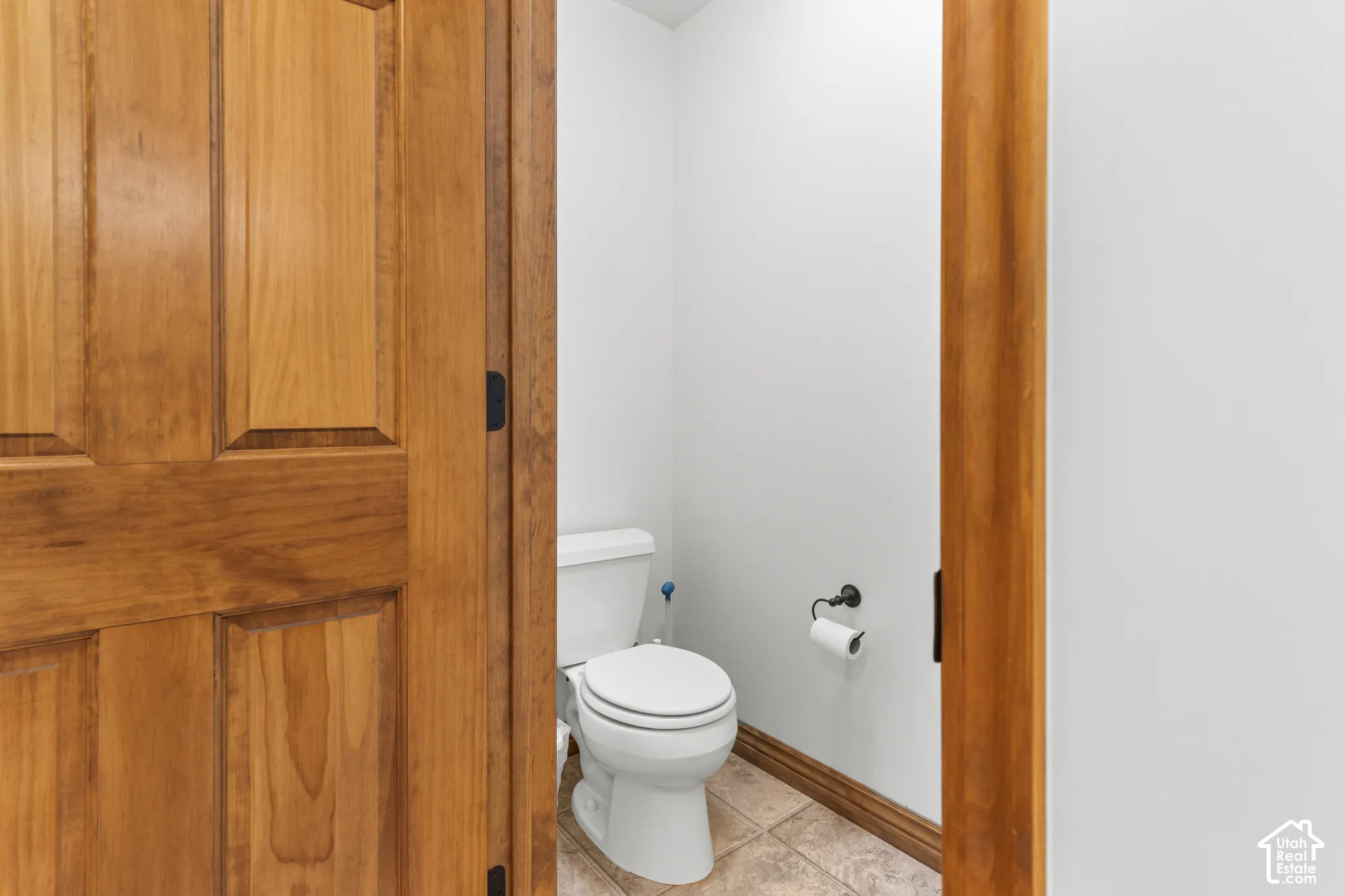 Solid wood-finish interior door featuring decorative paneling, porcelain commode, matte black hardware, and stone-finish tile flooring