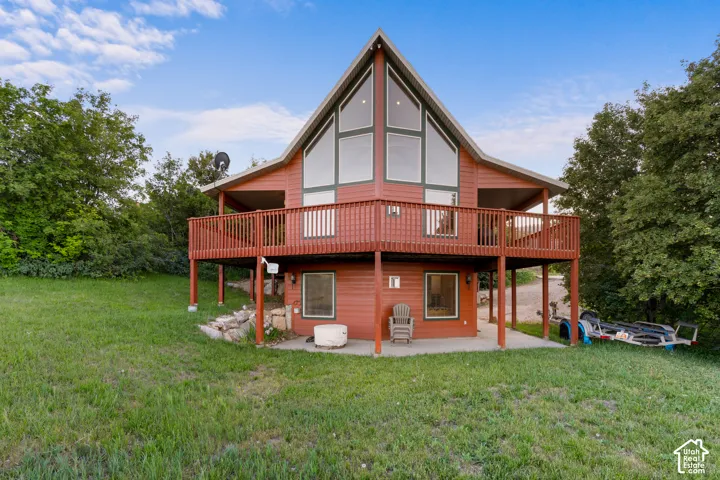 A-frame exterior featuring horizontal siding, expansive multi-pane glass windows, a wraparound wood deck, and a concrete patio