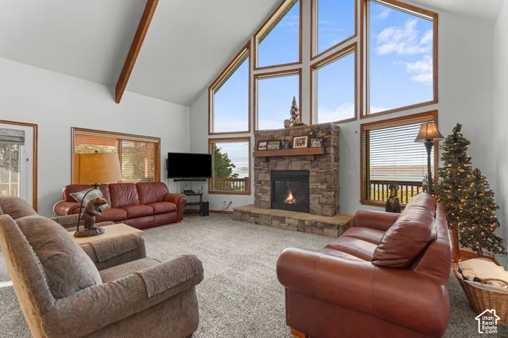 Vaulted ceilings with exposed timber beams, expansive floor-to-ceiling windows, and a floor-to-ceiling stone fireplace featuring a substantial wooden mantel