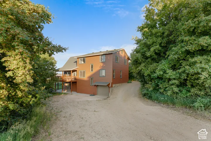 Three-story residence featuring horizontal siding, an attached garage, and a covered deck, situated on a secluded lot with dense mature landscaping