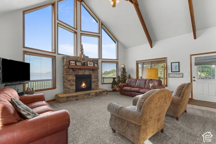 Vaulted ceiling with exposed wood beams, stone-clad fireplace with timber mantel, and expansive multi-pane windows