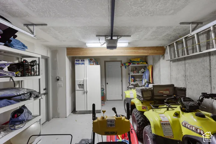 Garage space featuring concrete foundation walls, exposed wood ceiling beam, fluorescent lighting, and two entry doors