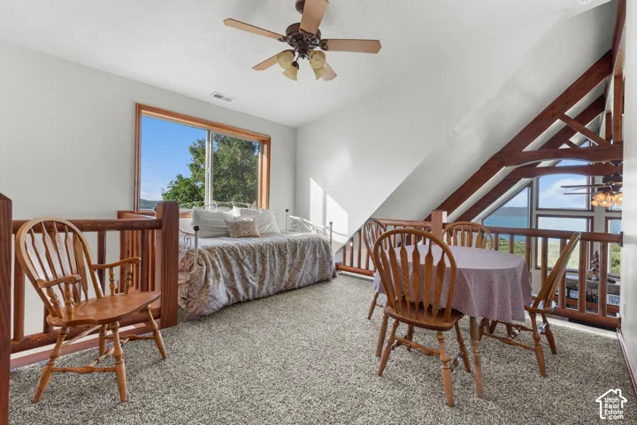 Vaulted ceiling with exposed wood beams, wood-frame windows, wood railing, and a ceiling fan