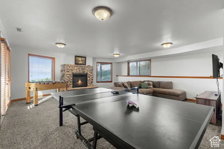 Floor-to-ceiling river rock fireplace, neutral wall-to-wall carpeting, multiple windows with wood-tone trim, and recessed and flush-mount ceiling lighting