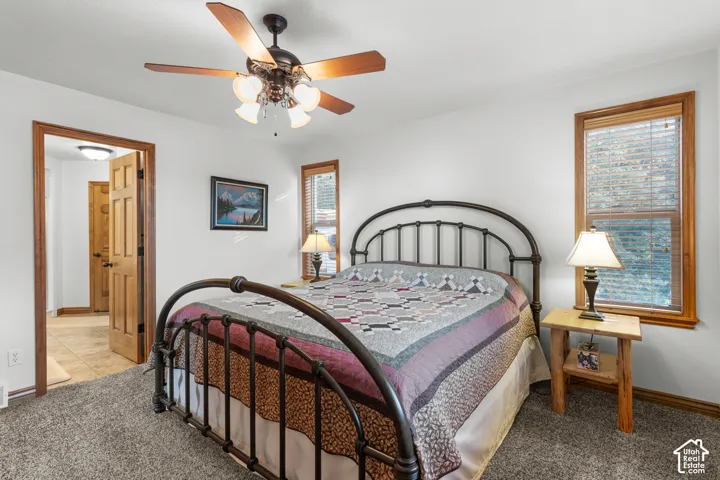 Neutral-toned carpeting, multi-pane windows with wood trim, six-panel wood door, and a ceiling fan with integrated multi-bulb lighting