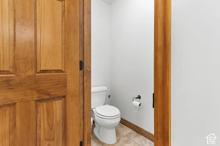 Solid wood-finish interior door featuring decorative paneling, porcelain commode, matte black hardware, and stone-finish tile flooring