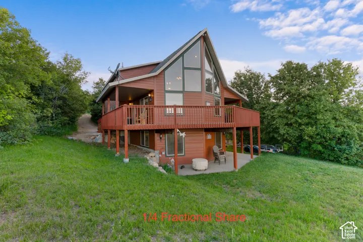 Multi-level wood-sided exterior featuring an A-frame roofline, expansive floor-to-ceiling windows, a wrap-around wooden deck, and a ground-level concrete patio