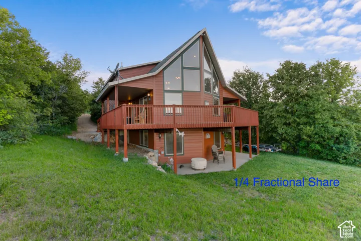 A-frame exterior featuring wood siding, expansive floor-to-ceiling windows, an elevated wraparound deck, and a ground-level concrete patio