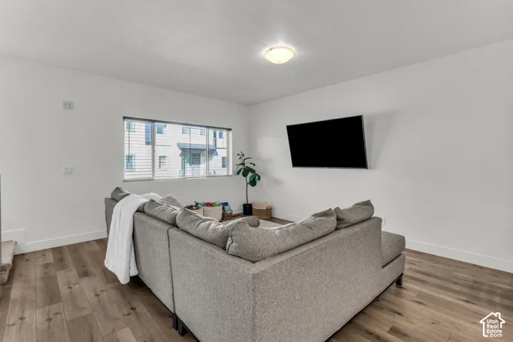 Neutral-toned room featuring wood-finish flooring, a large window with horizontal blinds, and a centered flush-mount ceiling light fixture