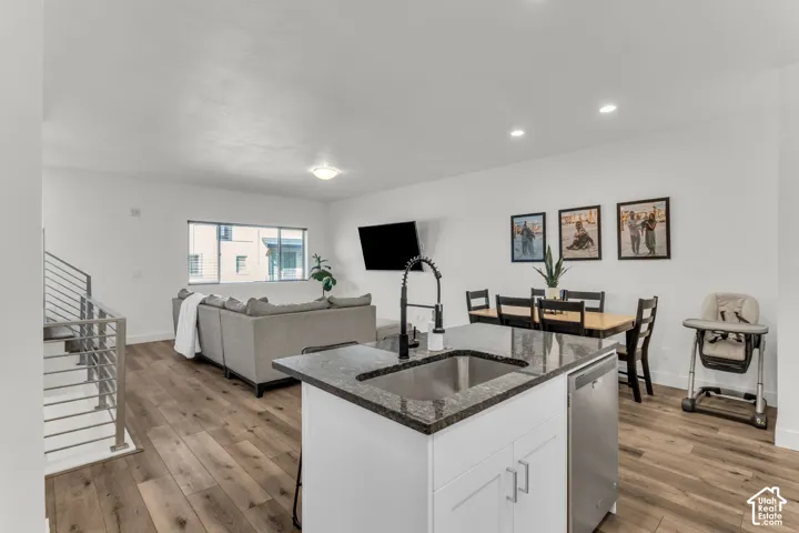 Kitchen island with a dark stone countertop, integrated stainless steel sink, and high-arc faucet, complemented by wood-finish flooring and a metal-rail staircase