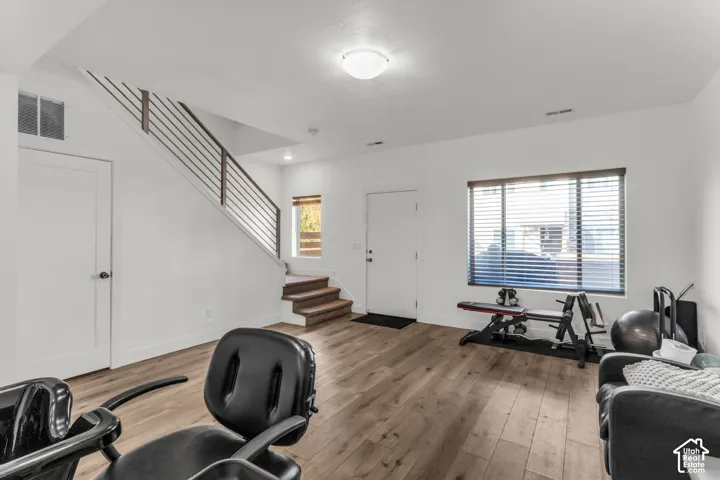 Open-concept space featuring wood-finish flooring, a staircase with horizontal metal railing, and large windows with blinds