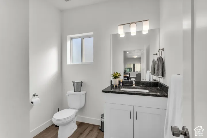 White vanity with dark stone countertop, integrated rectangular sink, wood-finish flooring, and three-light glass fixture