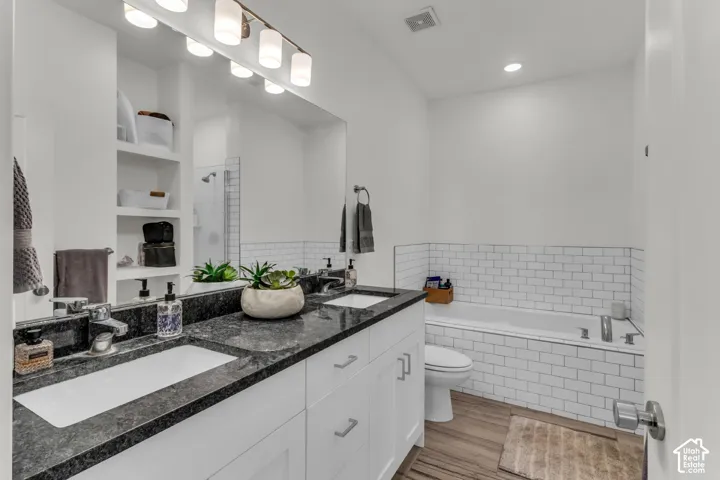 Double vanity featuring stone countertops and rectangular undermount sinks, complemented by built-in shelving, a full-width vanity mirror, and white subway tile surrounding the tub