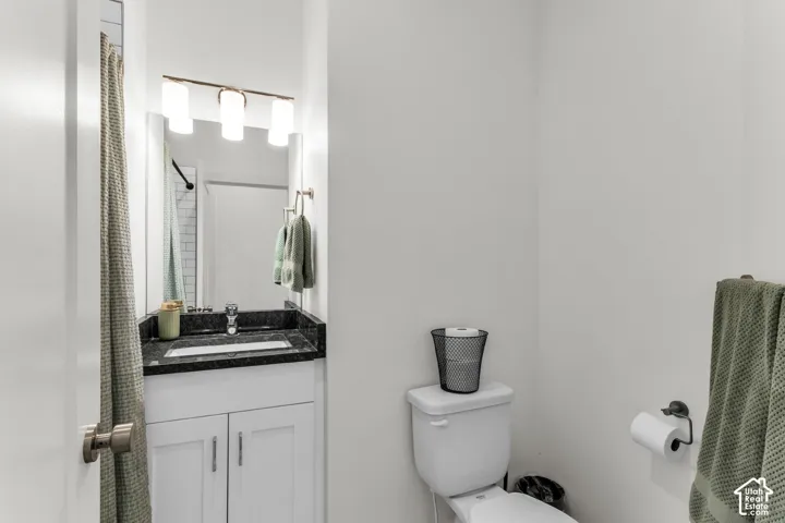 Bathroom featuring a vanity with dark stone-finish countertop, white cabinetry, three-light vanity fixture, and rectangular basin
