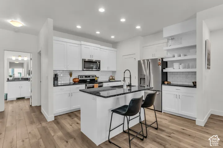 Kitchen featuring white shaker-style cabinetry, a contrasting island with dark countertops, white subway tile backsplash, stainless steel appliances, and wood-finish flooring