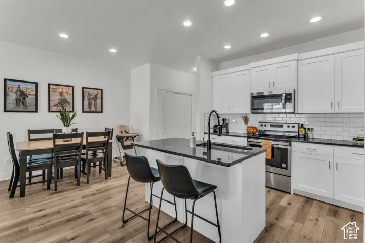 Kitchen featuring white shaker-style cabinetry, dark stone countertops, stainless steel appliances, a white subway tile backsplash, and wood-finish flooring