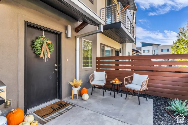 Modern exterior entrance featuring a concrete patio, horizontal wood-slat privacy fencing, and a metal-railing balcony