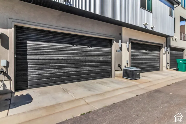 Multi-car garage with horizontal panel doors, stucco exterior siding, and metal corrugated upper-level cladding
