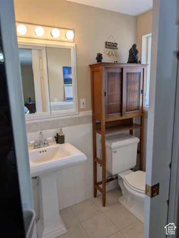 Pedestal sink with chrome dual-handle faucet, vanity mirror with integrated four-light fixture, tiled wall wainscoting, and ceramic tile flooring
