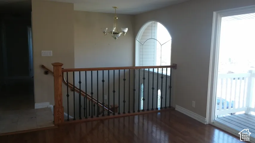 Staircase featuring wood handrails and matte black metal balusters, polished wood-finish flooring, an arched window, and an overhead multi-light chandelier