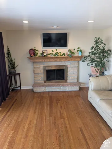 Stone fireplace surround with wood mantel, raised stone hearth, and wood-finish flooring