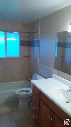 Bathroom featuring wood-finish vanity cabinetry, solid-surface countertop with integrated basin, tub-shower combination with tile surround, and tiled flooring