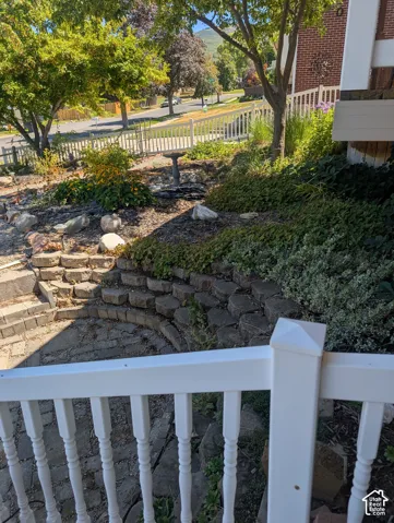 Tiered stone retaining wall, paved stone patio, white vinyl fencing, and mature landscaping